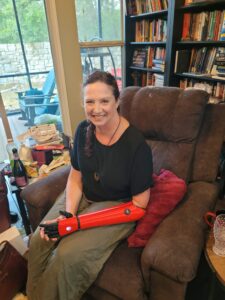 Julie sitting in a recliner in her living room with her red Hero Arm